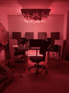 Regieraum eines Tonstudios mit Studiomonitoren, Akustikelementen und roter Beleuchtung