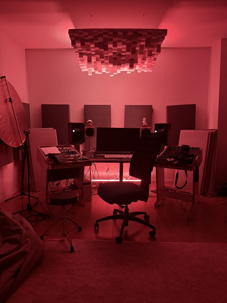 Regieraum eines Tonstudios mit Studiomonitoren, Akustikelementen und roter Beleuchtung